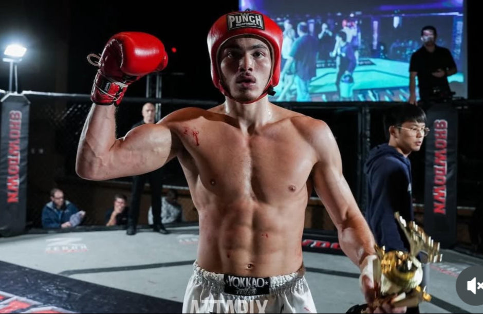 Boxer in a red helmet and red gloves flexing his arm on a boxing ring.