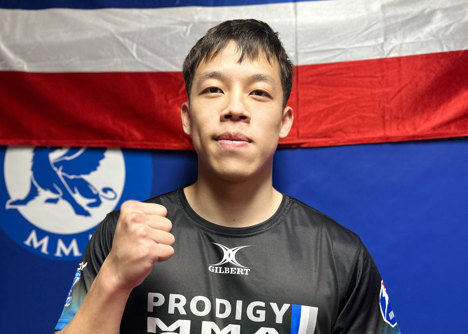 Person wearing a Prodigy MMA shirt in front of a flag with MMA branding.