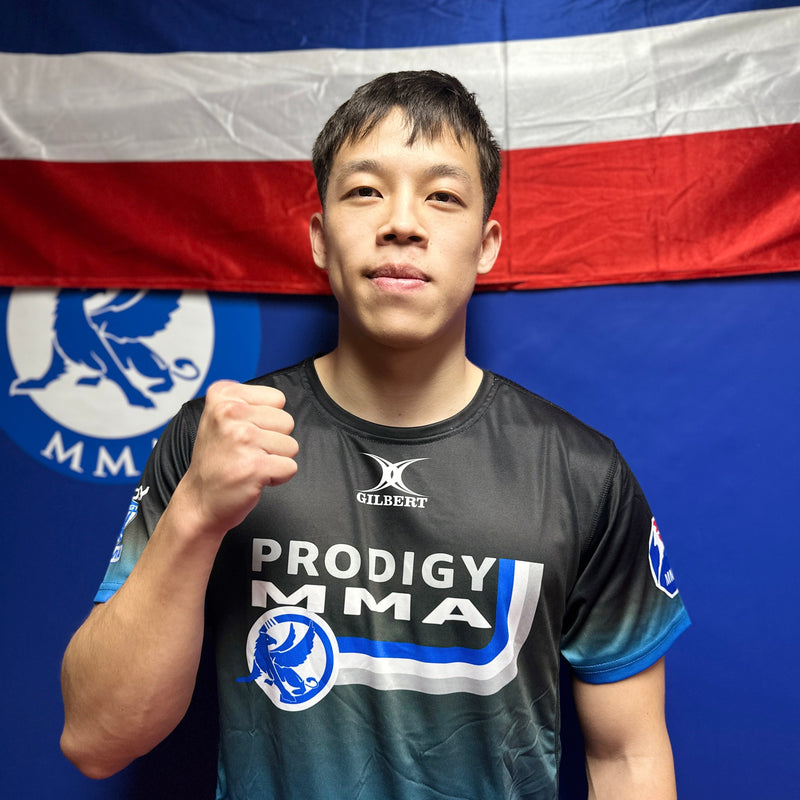 Person wearing a Prodigy MMA shirt in front of a flag with MMA branding.