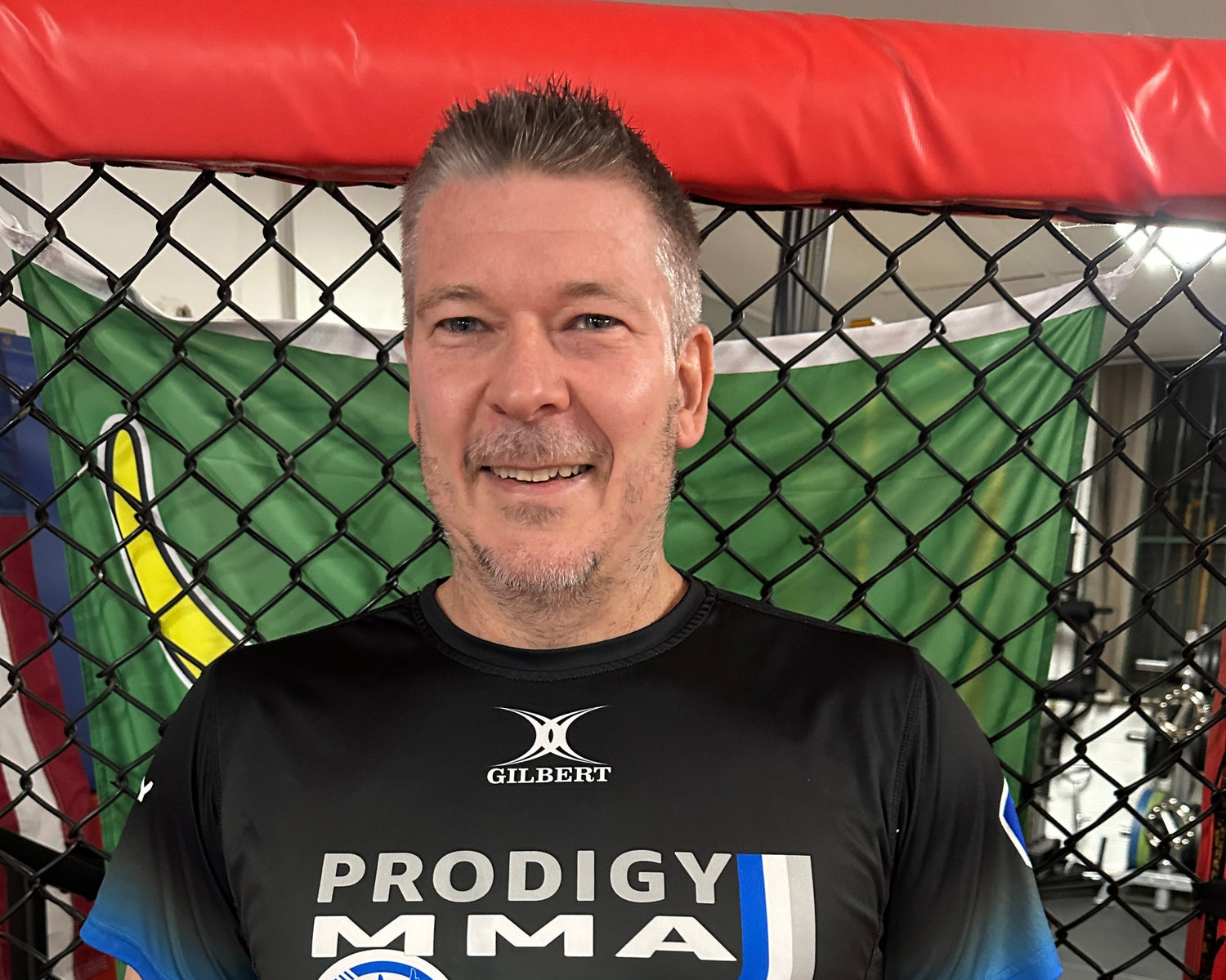 Man wearing a Prodigy MMA shirt in a cage fighting ring.