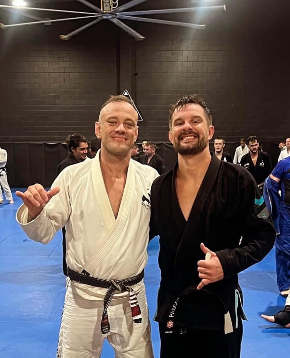 Two men in martial arts uniforms posing for a photo on a blue mat.
